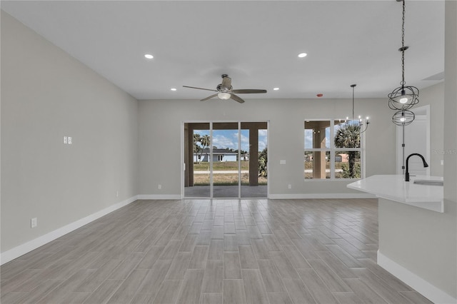 unfurnished living room featuring baseboards, light wood-type flooring, recessed lighting, ceiling fan with notable chandelier, and a sink