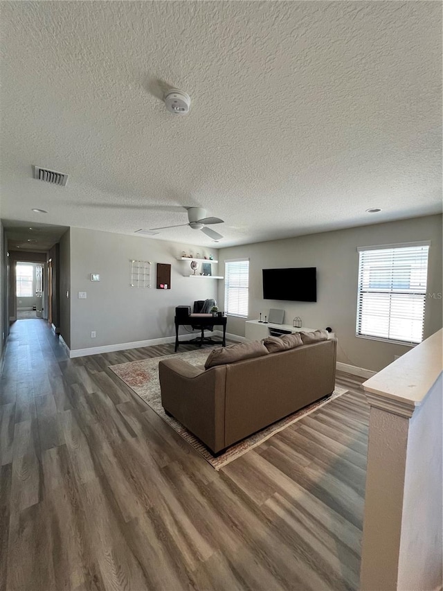 living room featuring a healthy amount of sunlight, a textured ceiling, dark wood-type flooring, and ceiling fan