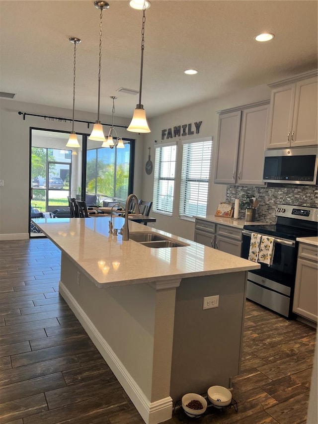 kitchen featuring stainless steel appliances, an island with sink, decorative light fixtures, a healthy amount of sunlight, and tasteful backsplash