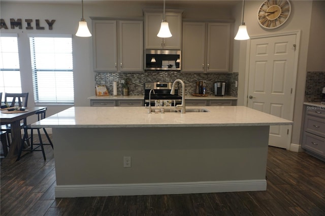 kitchen featuring stainless steel appliances, gray cabinets, light stone counters, backsplash, and a kitchen island with sink