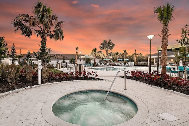 pool at dusk with a hot tub