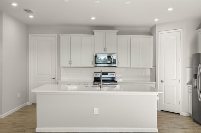 kitchen with white cabinetry, light hardwood / wood-style flooring, an island with sink, and appliances with stainless steel finishes