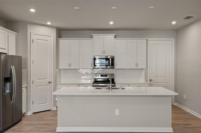 kitchen with sink, appliances with stainless steel finishes, a kitchen island with sink, white cabinets, and light wood-type flooring