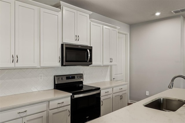 kitchen featuring light stone countertops, backsplash, stainless steel appliances, sink, and white cabinetry