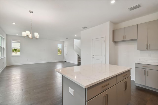 kitchen featuring light stone counters, gray cabinetry, an inviting chandelier, a center island, and dark hardwood / wood-style floors