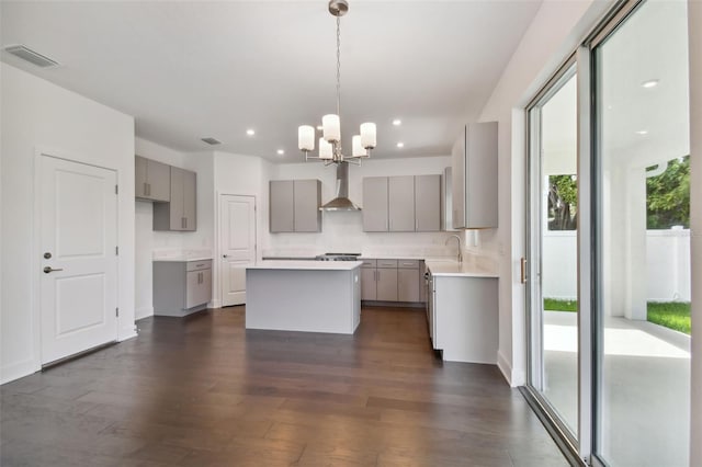 kitchen with wall chimney range hood, a chandelier, a center island, gray cabinets, and dark hardwood / wood-style floors