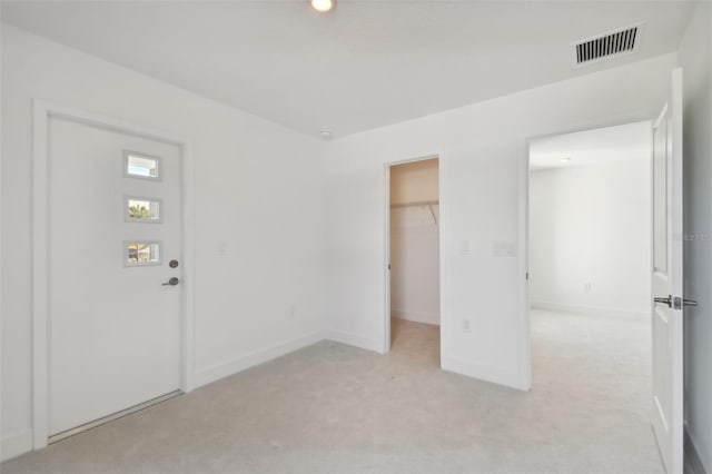 unfurnished bedroom featuring a walk in closet, a closet, and light colored carpet