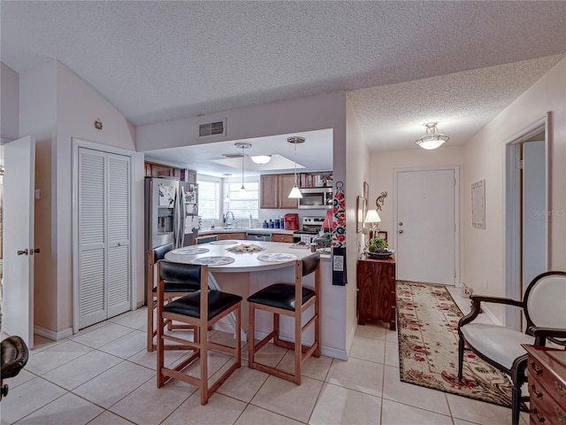 kitchen featuring lofted ceiling, sink, light tile patterned floors, stainless steel appliances, and a textured ceiling