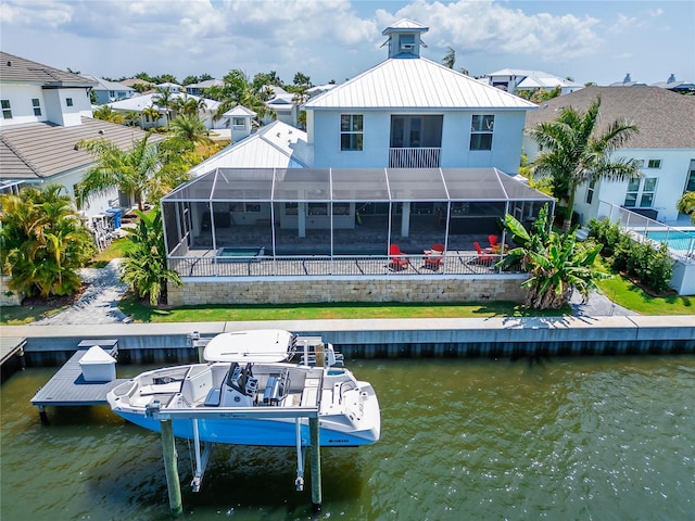 back of property with glass enclosure, a water view, and a patio area