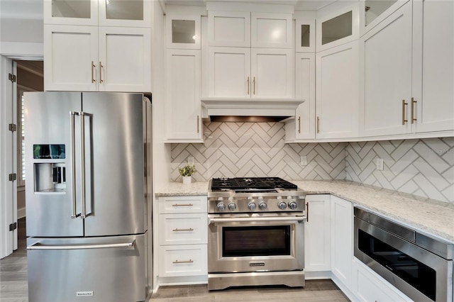 kitchen with premium appliances, tasteful backsplash, white cabinets, and hardwood / wood-style flooring