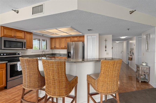 kitchen with appliances with stainless steel finishes, a textured ceiling, a breakfast bar, a center island, and light tile floors