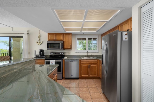 kitchen featuring appliances with stainless steel finishes, a textured ceiling, dark stone countertops, sink, and light tile floors