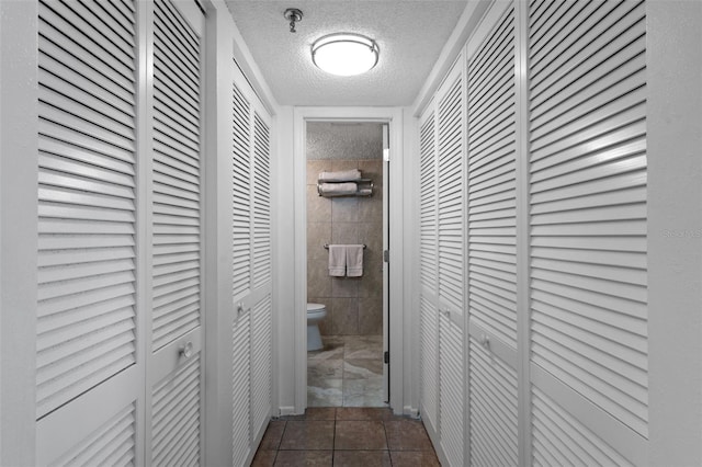 hallway with dark tile flooring, tile walls, and a textured ceiling