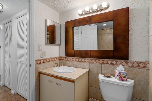 bathroom featuring toilet, oversized vanity, tile walls, and a textured ceiling