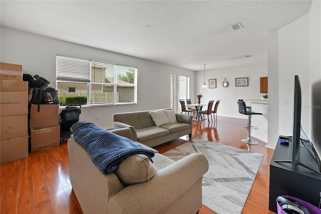 living area featuring visible vents, light wood-style flooring, and a textured ceiling