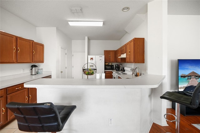 kitchen featuring white appliances, a kitchen breakfast bar, a peninsula, under cabinet range hood, and light countertops