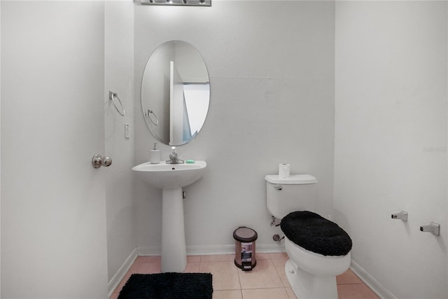 half bath with toilet, tile patterned floors, a sink, and baseboards