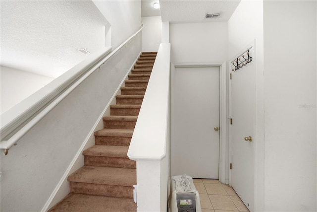 stairs featuring tile patterned floors, visible vents, and a textured ceiling