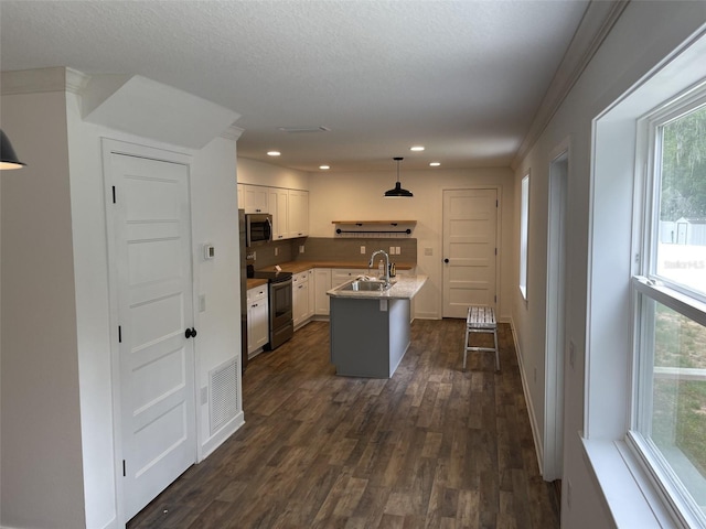 kitchen featuring pendant lighting, appliances with stainless steel finishes, dark wood-type flooring, white cabinets, and a sink