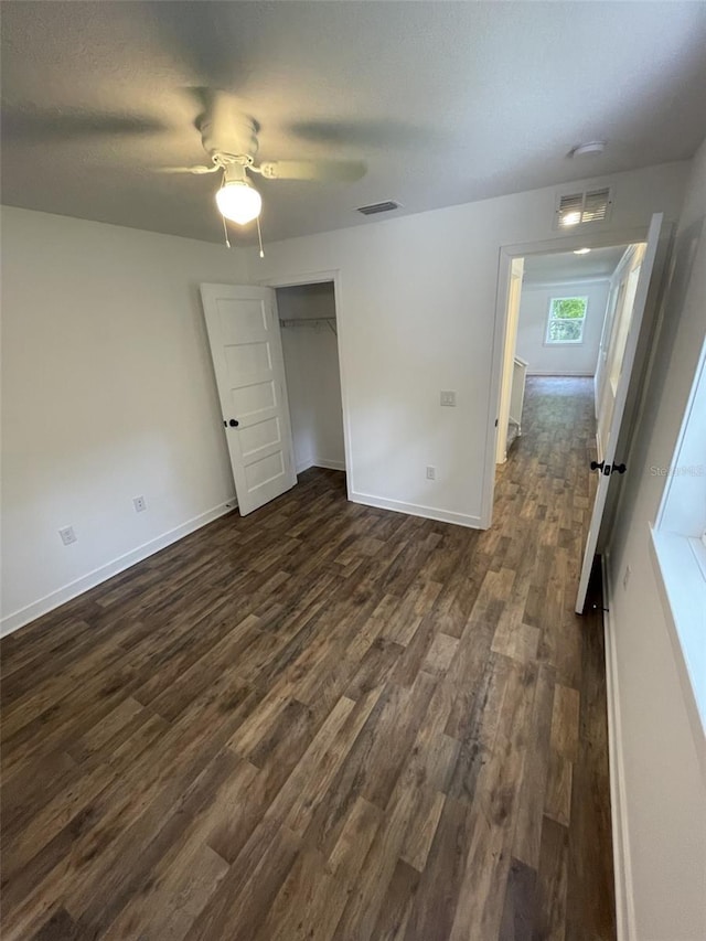 unfurnished bedroom with dark wood-type flooring, a ceiling fan, visible vents, and baseboards