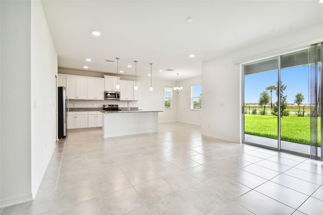 kitchen featuring white cabinets, decorative light fixtures, an island with sink, and appliances with stainless steel finishes