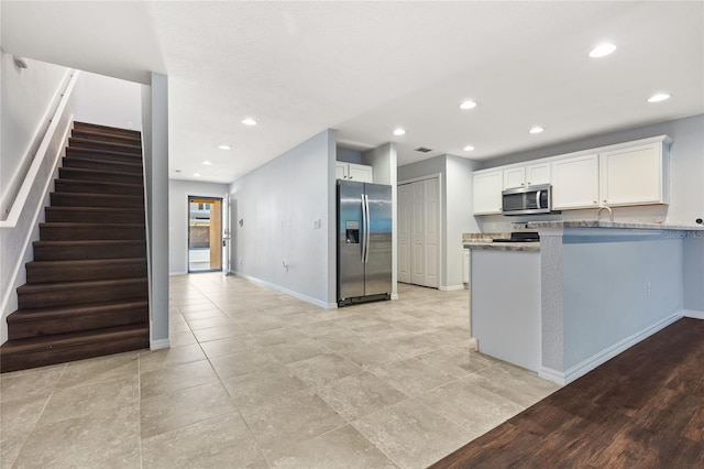 kitchen featuring kitchen peninsula, white cabinets, stainless steel appliances, light hardwood / wood-style floors, and stone counters