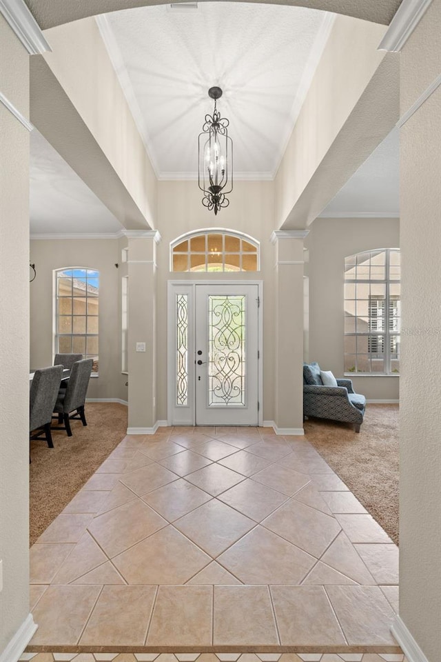 entrance foyer with a chandelier, ornamental molding, decorative columns, and light tile floors