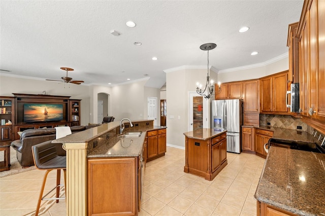 kitchen featuring sink, ceiling fan with notable chandelier, backsplash, stainless steel appliances, and an island with sink