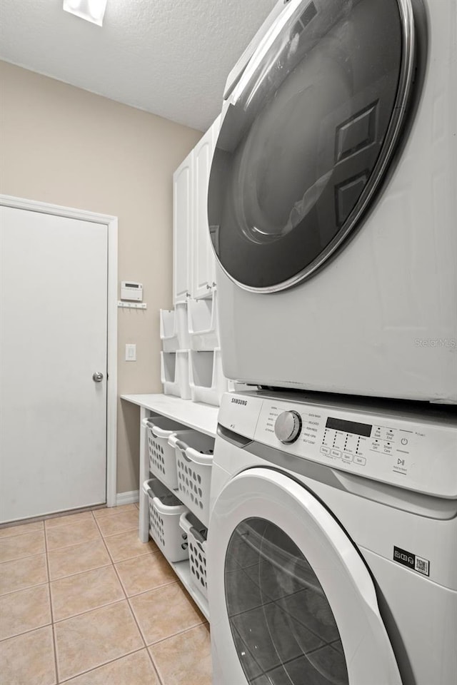 clothes washing area with stacked washer / dryer, cabinets, and light tile flooring