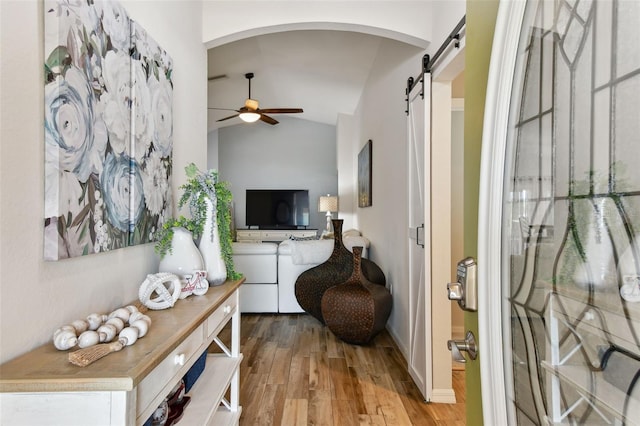 corridor featuring a barn door, light hardwood / wood-style flooring, and vaulted ceiling