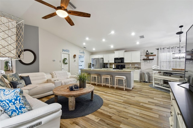 living room featuring vaulted ceiling, ceiling fan, sink, and light hardwood / wood-style flooring