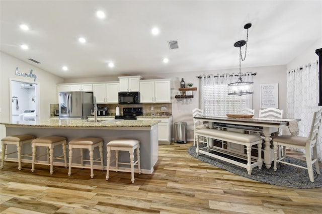 kitchen with white cabinetry, black appliances, tasteful backsplash, a kitchen island with sink, and light wood-type flooring