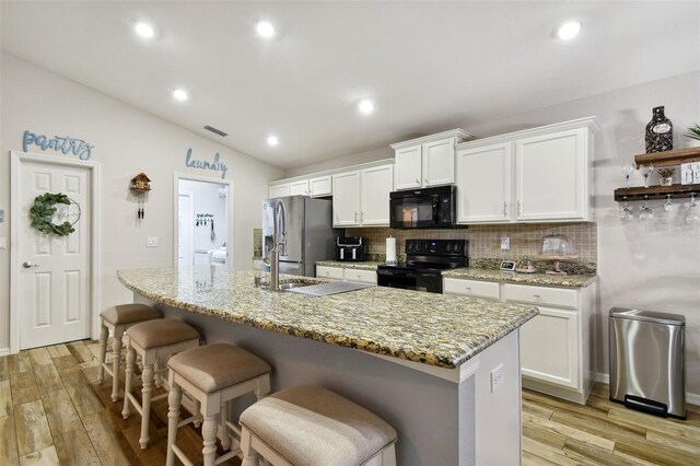 kitchen with vaulted ceiling, black appliances, tasteful backsplash, white cabinetry, and light wood-type flooring