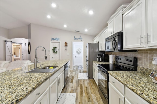 kitchen with a barn door, light hardwood / wood-style floors, black appliances, lofted ceiling, and tasteful backsplash