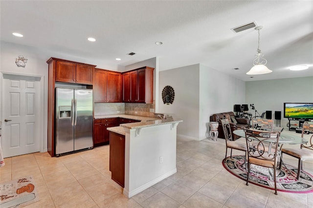 kitchen featuring light stone countertops, tasteful backsplash, kitchen peninsula, stainless steel fridge, and pendant lighting