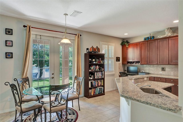 kitchen featuring pendant lighting, sink, tasteful backsplash, light tile patterned flooring, and light stone counters