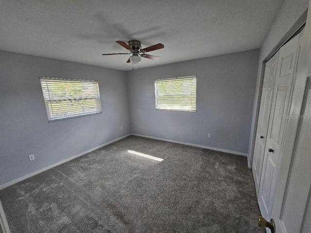 unfurnished bedroom featuring dark carpet, multiple windows, and ceiling fan