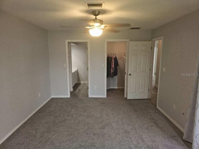 unfurnished bedroom with ceiling fan, ensuite bath, a walk in closet, carpet, and a textured ceiling