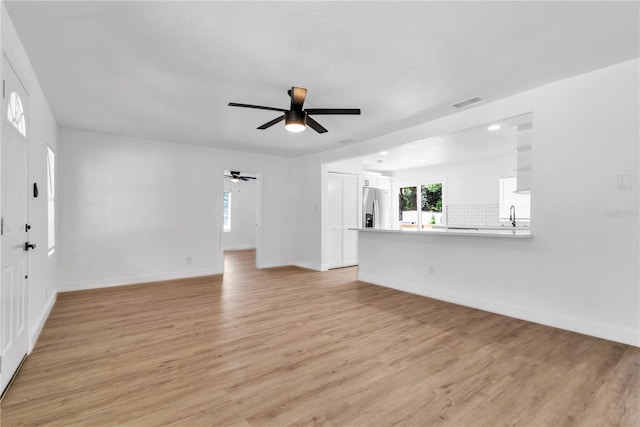 unfurnished living room with visible vents, baseboards, ceiling fan, light wood-style floors, and a sink