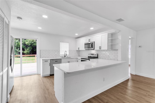 kitchen with white cabinets, stainless steel appliances, kitchen peninsula, and light hardwood / wood-style floors