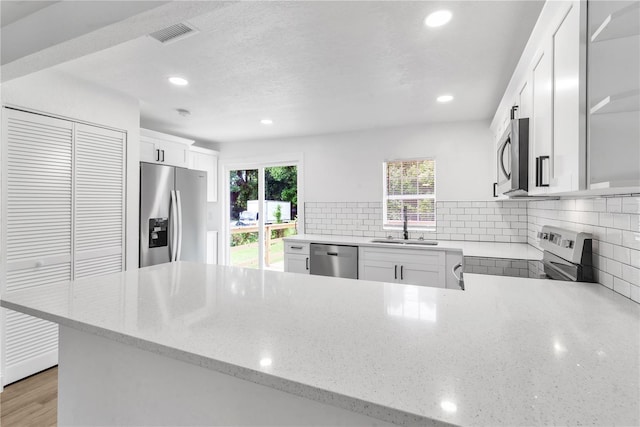 kitchen with decorative backsplash, appliances with stainless steel finishes, light stone countertops, white cabinets, and light hardwood / wood-style floors