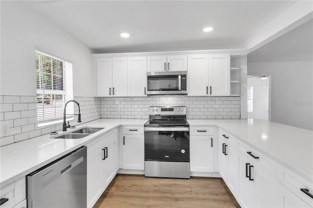 kitchen with open shelves, appliances with stainless steel finishes, white cabinetry, a sink, and a peninsula