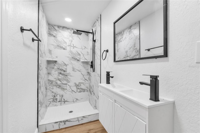 bathroom featuring hardwood / wood-style floors, tiled shower, and vanity