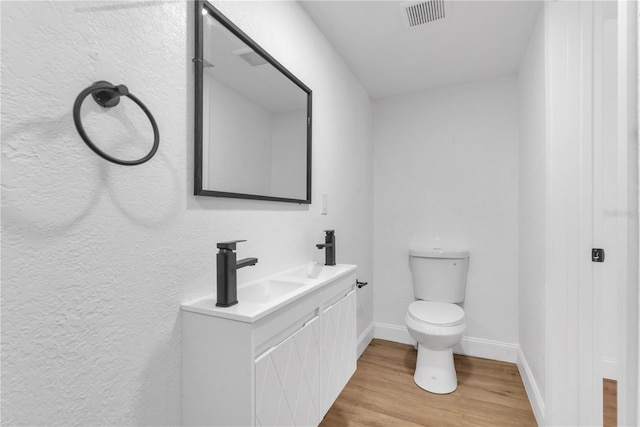 bathroom with baseboards, visible vents, toilet, wood finished floors, and a sink