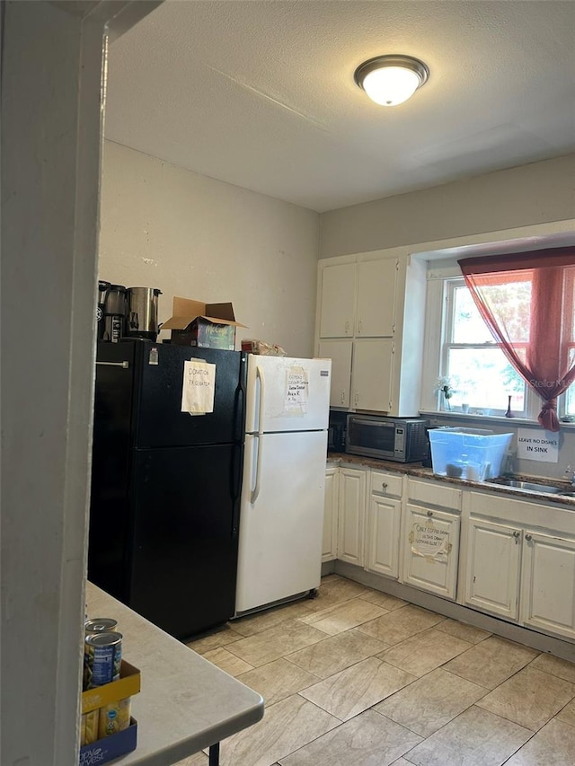 kitchen featuring white fridge, black fridge, light tile flooring, white cabinetry, and sink