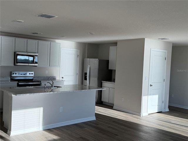 kitchen featuring hardwood / wood-style floors, sink, a kitchen island with sink, light stone counters, and stainless steel appliances