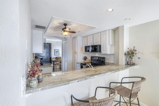 kitchen with white cabinetry, black appliances, a kitchen bar, a raised ceiling, and ceiling fan