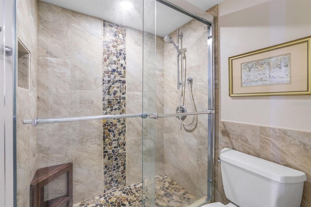 bathroom featuring tile walls, toilet, and a shower with shower door