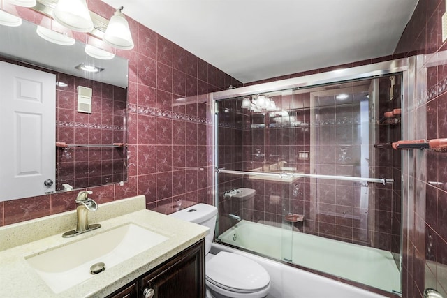 full bathroom featuring combined bath / shower with glass door, tile walls, vanity, and toilet