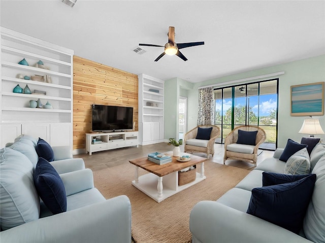 living room with built in features, ceiling fan, and wood walls